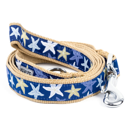 Light-colored starfish illustrations on navy ribbon nylon dog leash, coiled with tan backing